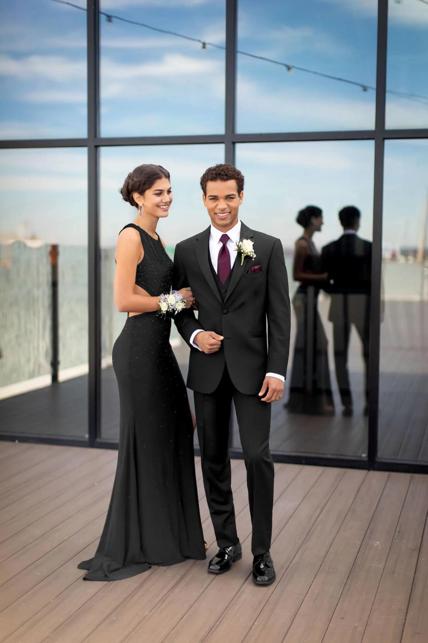 Model wearing black suit standing next to female model wearing a black gown